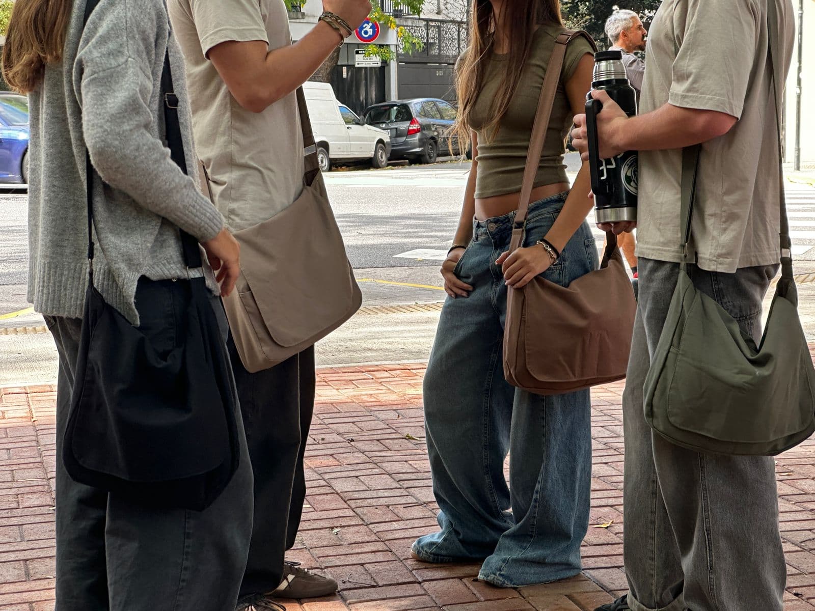 Cuatro personas en una vereda de la ciudad, cada una con un morral KOAL colgado al hombro: negro, beige, marrón y verde