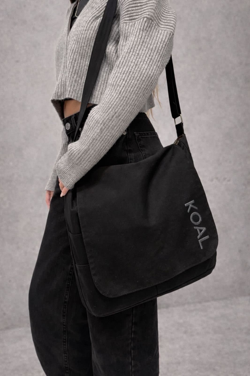 Persona con un morral KOAL negro colgado al hombro, sobre fondo gris de estudio